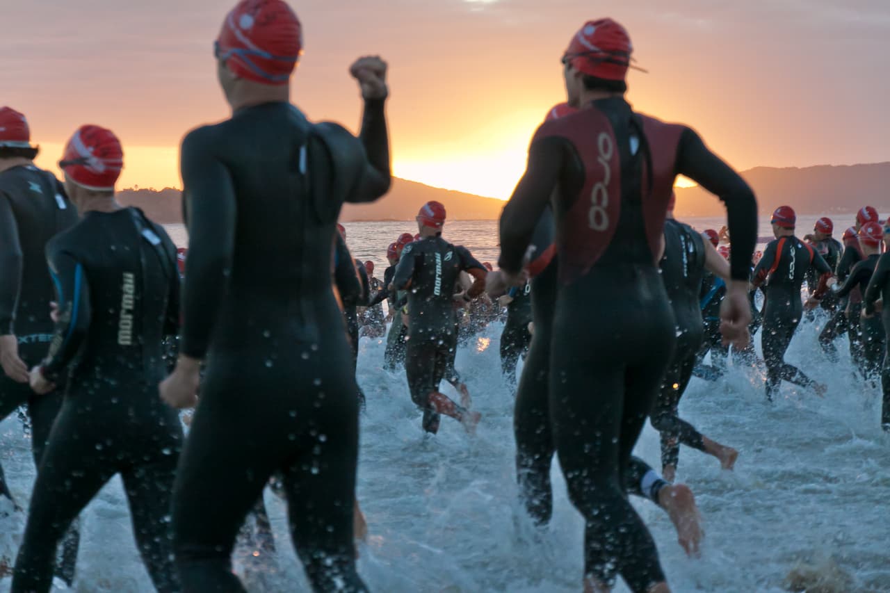 Triatleten in wetsuit lopen bij zonsopkomst het water in